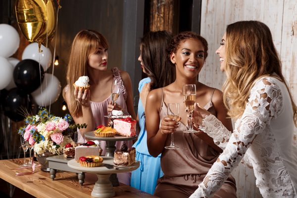 Four beautiful girls resting at party. Four young beautiful girls in dresses holding glasses with champagne, speaking, smiling, laughing, resting at party.